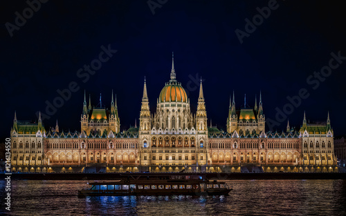 Obraz na płótnie illuminated Hungarian Parliament Building during the blue hour, with a boat cruising on the Danube River w salonie
