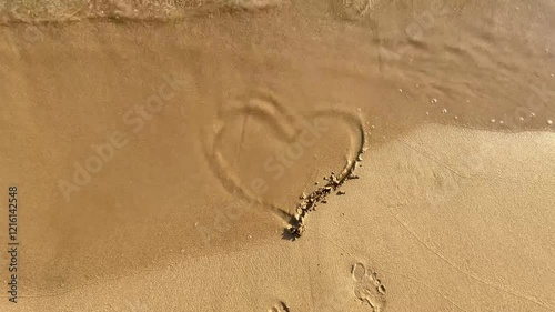 A heart drawn on the sand is washed away by the wave. Sandy beach. Summer vacations by the sea. Valentine's day, honeymoon and love concept