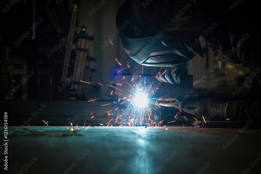 a person wearing a welding mask works on metal with a welding torch, creating sparks through the welding process