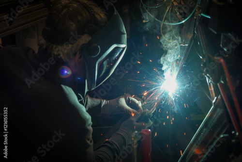 Obraz na płótnie a person wearing a welding mask works on metal with a welding torch, creating sparks through the welding process w salonie