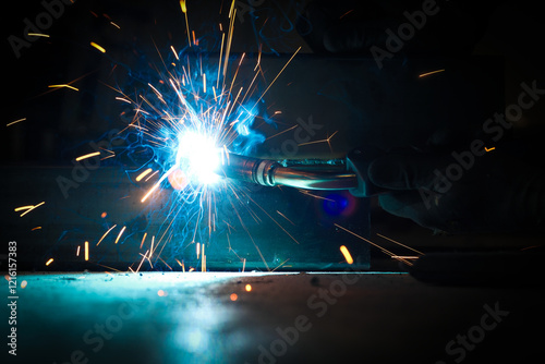 a person wearing a welding mask works on metal with a welding torch, creating sparks through the welding process