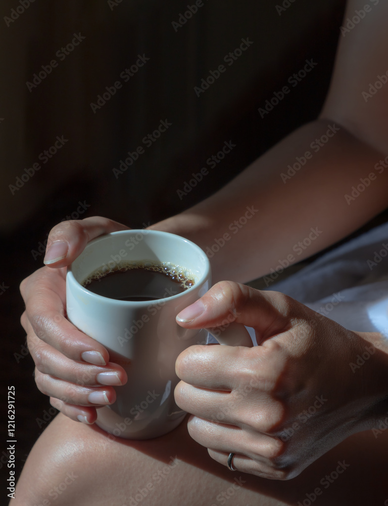 Close up of Comforting cozy female hands holding a coffee glass with the morning sunlight that shines through. Light and Shadow, use it as your Wallpaper, Poster and Space for text, Selective focus.
