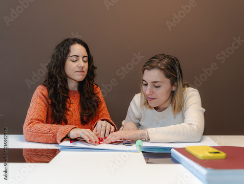 Canvas-taulu Blind woman guiding her friend through a tactile Braille book, promoting inclusi