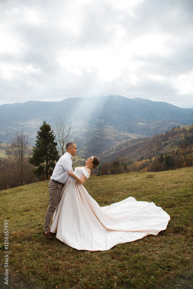 couple standing against the backdrop of a picturesque mountain landscape. A man and a woman are hugging, the woman is wearing a long light dress that flows beautifully along the ground. couple standing against the backdrop of a picturesque mountain landscape. A man and a woman are hugging, the woman is wearing a long light dress that flows beautifully along the ground.