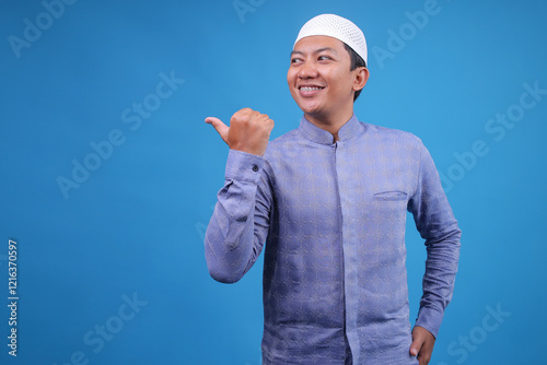 Portrait of Adult Asian Musllim Man Pointing Finger Aside Isolated on Blue Background
 photo