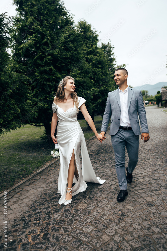 couple walking along a paved path. Trees and a stone wall are visible in the background. couple walking along a paved path. Trees and a stone wall are visible in the background.