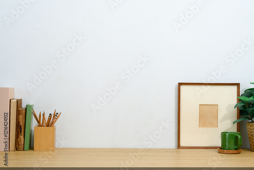 Rustic workspace with pencil holder, vintage books, a coffee mug, and picture frame against white wall