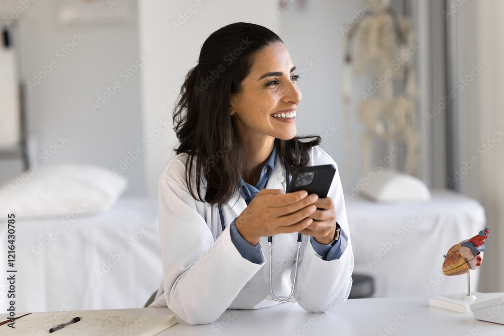 Easy communication on distance. Happy cheerful young lady doctor gp sit at work office table hold cellphone glad of giving help assistance to patient remotely get good news in email enjoy using device Easy communication on distance. Happy cheerful young lady doctor gp sit at work office table hold cellphone glad of giving help assistance to patient remotely get good news in email enjoy using device