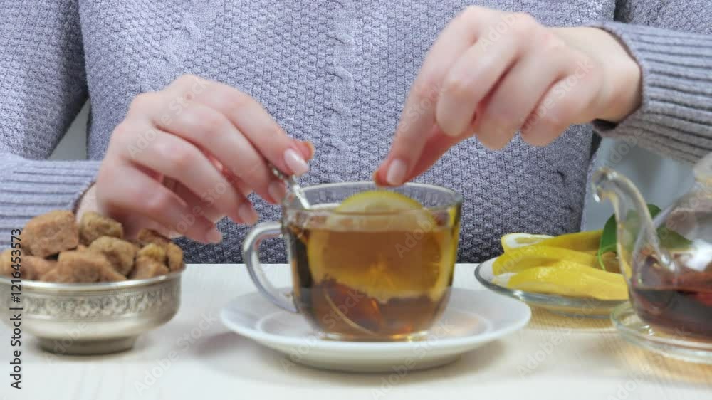 A young girl, throwing a lemon into a cup with tea, improving the taste of the drink, stirring with a spoon, in a composition with dessert and fruit.Close-up. Slow motion. A young girl, throwing a lemon into a cup with tea, improving the taste of the drink, stirring with a spoon, in a composition with dessert and fruit.Close-up. Slow motion.