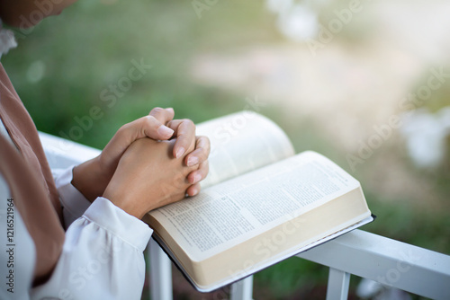 Hands folded in prayer on a Holy Bible in garden concept for faith