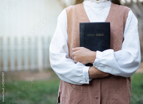 Asian woman holding Bible and praying in the garden.