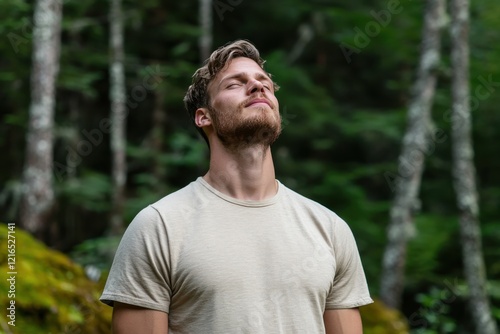 A tranquil man stands in a lush forest, eyes closed, embracing the serene surroundings, showcasing a connection with nature and the beauty of outdoor life.