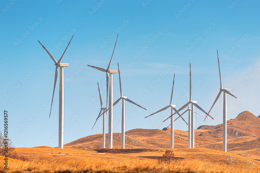 Wind turbines standing on a dry hilly landscape, generating renewable energy under a clear blue sky Wind turbines standing on a dry hilly landscape, generating renewable energy under a clear blue sky