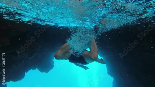 A swimmer without a mask dives in the clear blue waters of the Mediterranean Sea. Diving among the rocks