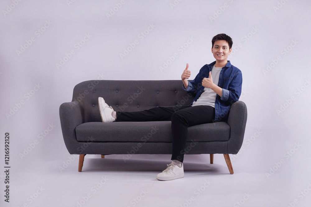 Full body image of young Asian man posing on sofa on white background Full body image of young Asian man posing on sofa on white background