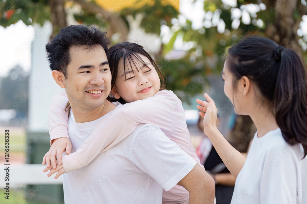 Delighted father carrying daughter on his back while mother shares a moment of joy outdoors Delighted father carrying daughter on his back while mother shares a moment of joy outdoors