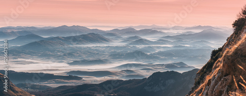 Obraz na płótnie Breathtaking panoramic view of a mountain range at sunrise, with pink sky and layers of fog creating a serene atmosphere w salonie