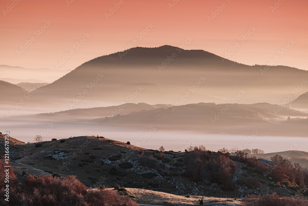 Low lying fog covering layers of hills at dawn with a beautiful orange sky