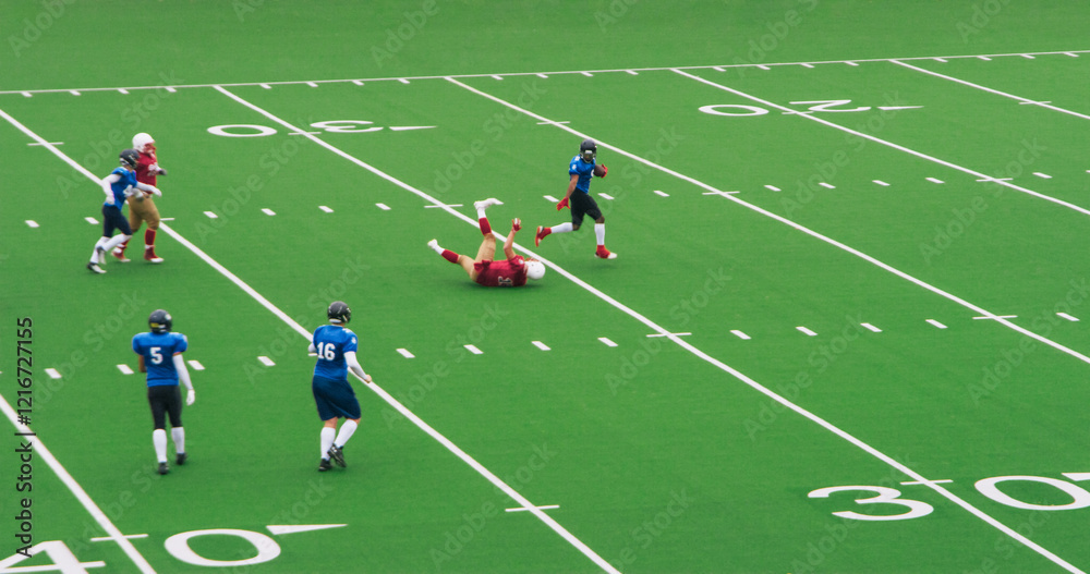 American Football Clash Unfolds as Professional Male Athletes Tackle Competition on a Green Outdoors Field. Agile Blue Footballer Running Away with the Ball From a Fallen Competitor American Football Clash Unfolds as Professional Male Athletes Tackle Competition on a Green Outdoors Field. Agile Blue Footballer Running Away with the Ball From a Fallen Competitor