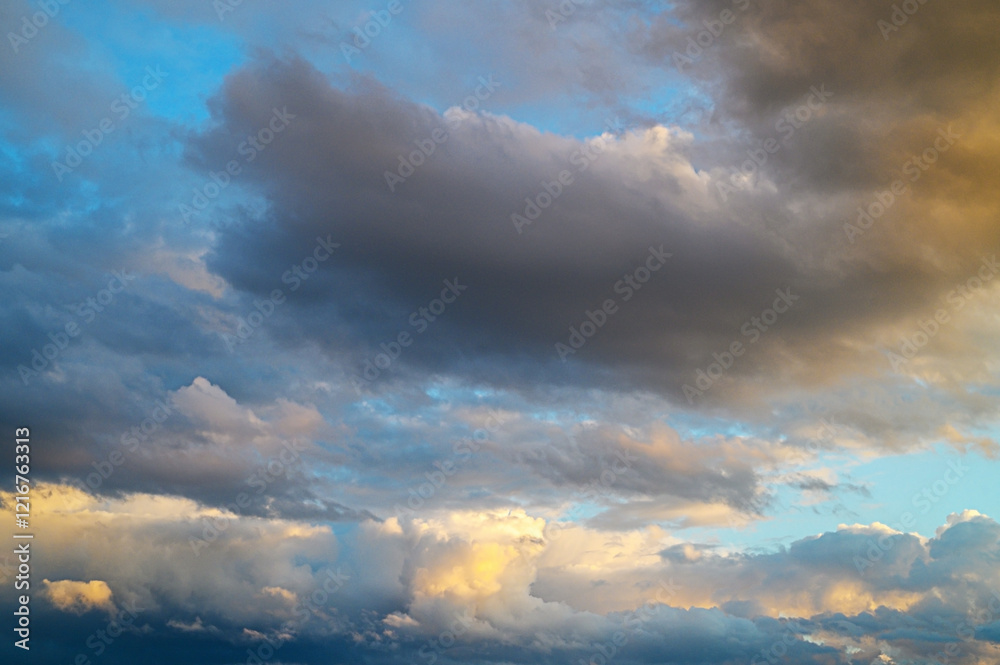 Fototapeta premium Shifting clouds dance across the vibrant sky at sunset, painting the horizon with golden hues