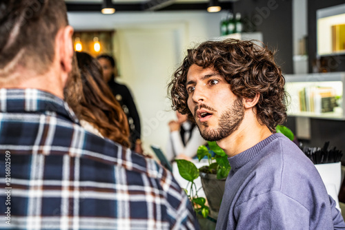 Young man with curly hair expressing surprise or confusion in a casual indoor setting. Interaction and emotions captured in a social environment with contemporary decor.