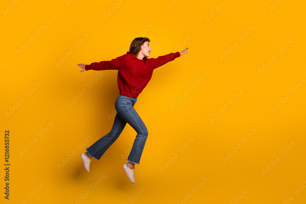 Fototapeta premium Energetic young woman in a red sweater jumping joyfully against a vibrant yellow background