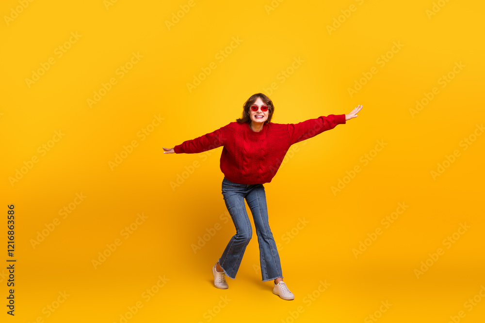 Smiling young woman in red sweater and jeans playfully posing against a vibrant yellow background Smiling young woman in red sweater and jeans playfully posing against a vibrant yellow background