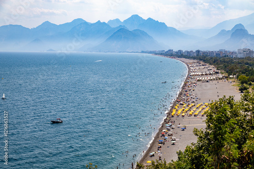 Fototapeta Naklejka Na Ścianę i Meble -  View of Konyaalti beach full of people and blue mountains in the background at summer daytime at Antalya, Turkey	