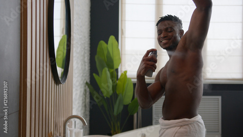 Smiling shirtless African American man applying deodorant antiperspirant in armpit get ready looking in bathroom mirror male everyday hygiene hyperhidrosis treatment sweat protection daily skincare
