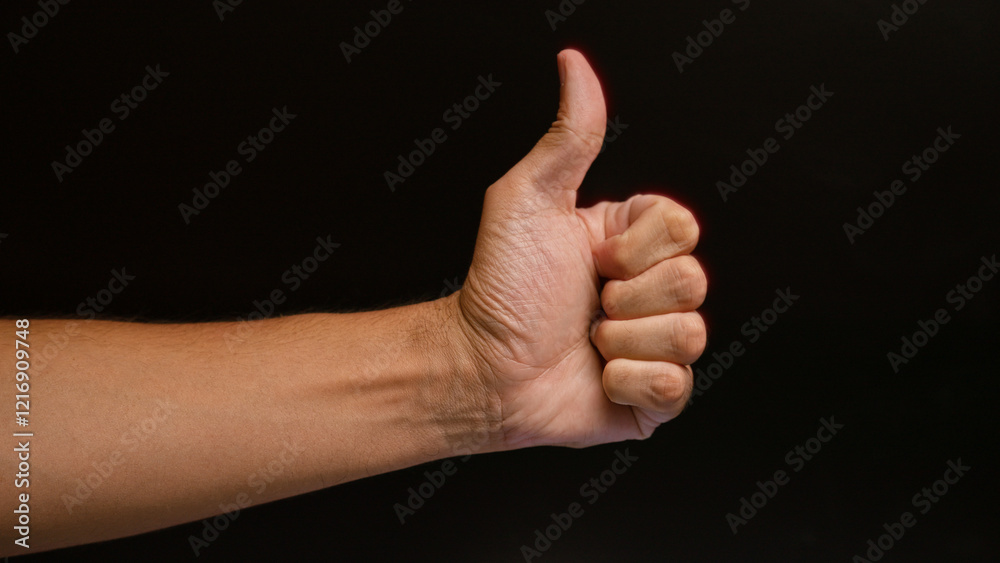 Man showing a thumbs-up sign with a close-up of his hand against a dark background, illustrating approval or positivity Man showing a thumbs-up sign with a close-up of his hand against a dark background, illustrating approval or positivity