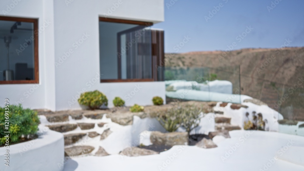 Naklejka premium Modern house exterior with blurred white walls, outdoor steps, and surrounding greenery in a sunny setting with a blurred background view of hills and clear sky.
