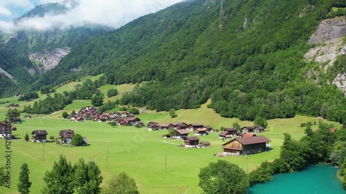 Drone footage of turquoise clear lake Lungern or Lungerersee in Switzerland in summer sunny day with village and green meadow