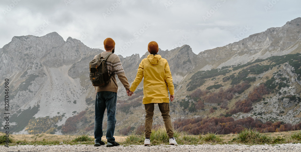 Fototapeta premium Breathtaking mountain landscape with happy young couple holding their hands. Rear view. Travel around the world concept. Montenegro country, Durmitor National Park. Saddle Pass in autumn season