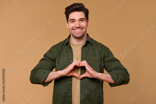 A cheerful man smiles and forms a heart shape with his hands against a warm, inviting background photo