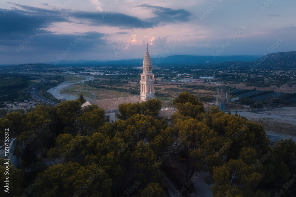 Fototapeta premium Aerial view of a historic church tower in a scenic valley during sunset, surrounded by trees and a meandering river
