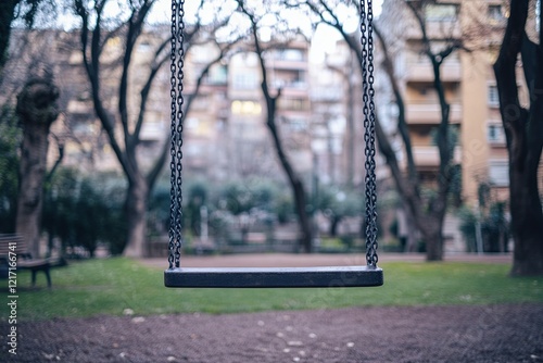 A solitary park swing in a small urban playground surrounded by blurred buildings. picture