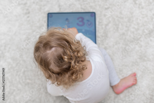 Obraz na płótnie Little girl using a tablet in a cozy home environment. A small child playing with a tablet in a comfortable home setting. w salonie