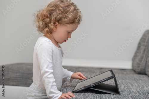 Obraz na płótnie Little girl using a tablet in a cozy home environment. A small child playing with a tablet in a comfortable home setting. w salonie