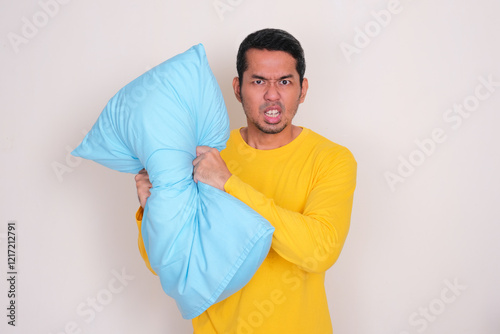 Adult Asian man crushing a pillow showing angry expression photo