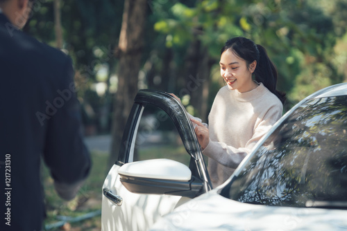 A Moment of Courtesy: A friendly exchange unfolds as a woman smiles and opens her car door for a man standing nearby, showcasing a warm and polite interaction.