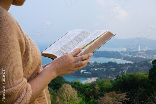 Christian woman holds a Bible in her hand Read the Bible on an island with a sea beach and many buildings. Concept for faith, spirituality and religion. peace hope