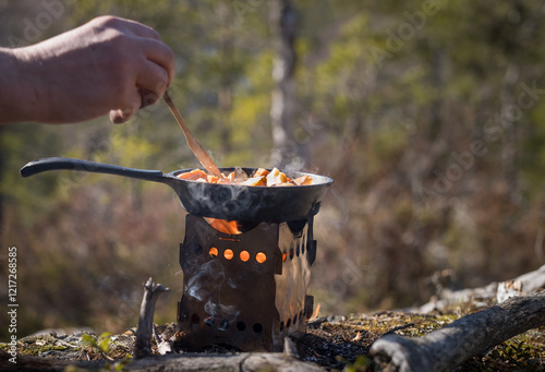 Canvas Print Male hand stirring in a frying pan over a hobo stove in the forest
