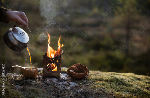 Coffee brewed on a firebox is poured into a wooden cup in a forest landscape