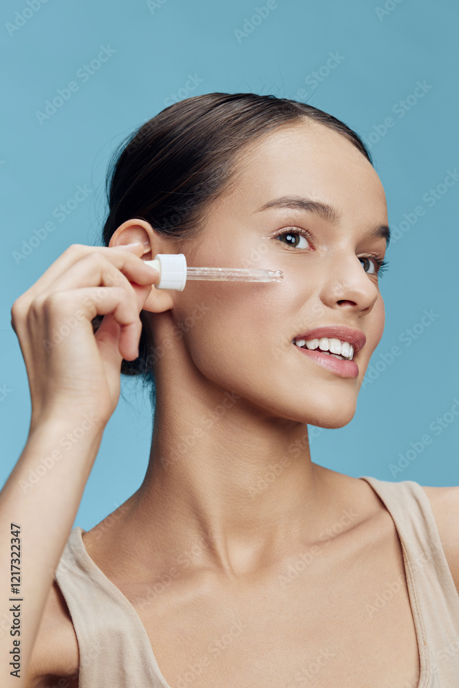 Smiling young woman applying skincare serum to her face against a light blue background, promoting healthy skin and beauty routines Smiling young woman applying skincare serum to her face against a light blue background, promoting healthy skin and beauty routines