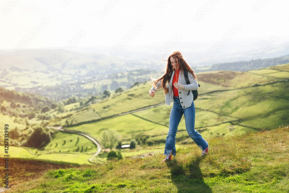 Fototapeta premium Woman hiking on a hillside overlooking a lush green valley during a sunny day