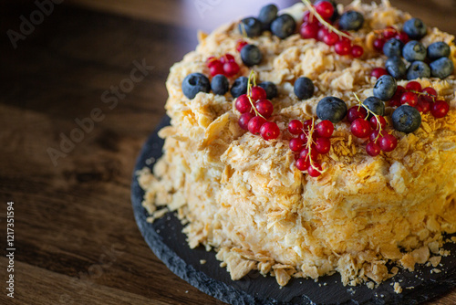 Delightful dessert with layers of cake topped with fresh berries and red currants on a wooden table