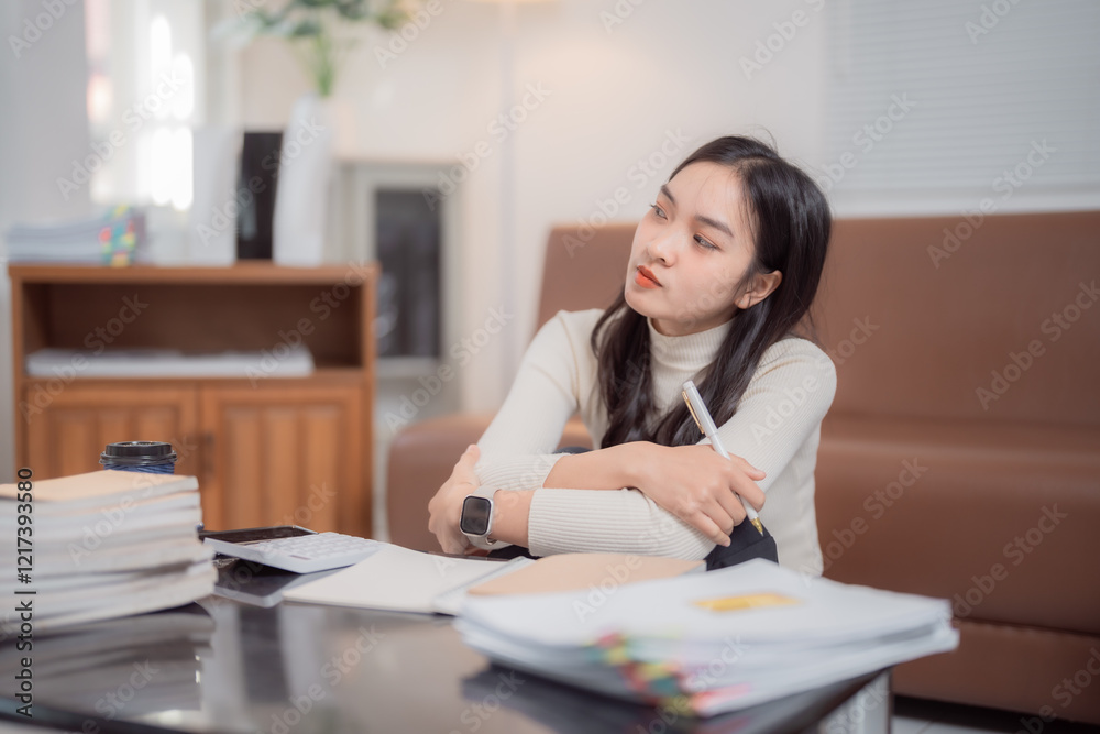Pensive asian businesswoman is sitting on the floor in her living room, taking a break from working with documents and calculator, holding a pen and looking away Pensive asian businesswoman is sitting on the floor in her living room, taking a break from working with documents and calculator, holding a pen and looking away
