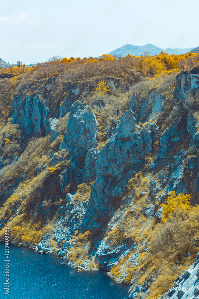 Obraz premium Infrared photography, a landscape with a body of water at the bottom and a rocky cliff. The cliff has vegetation with autumn-colored trees