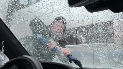 Man removes ice from car windshield during winter morning in urban area
