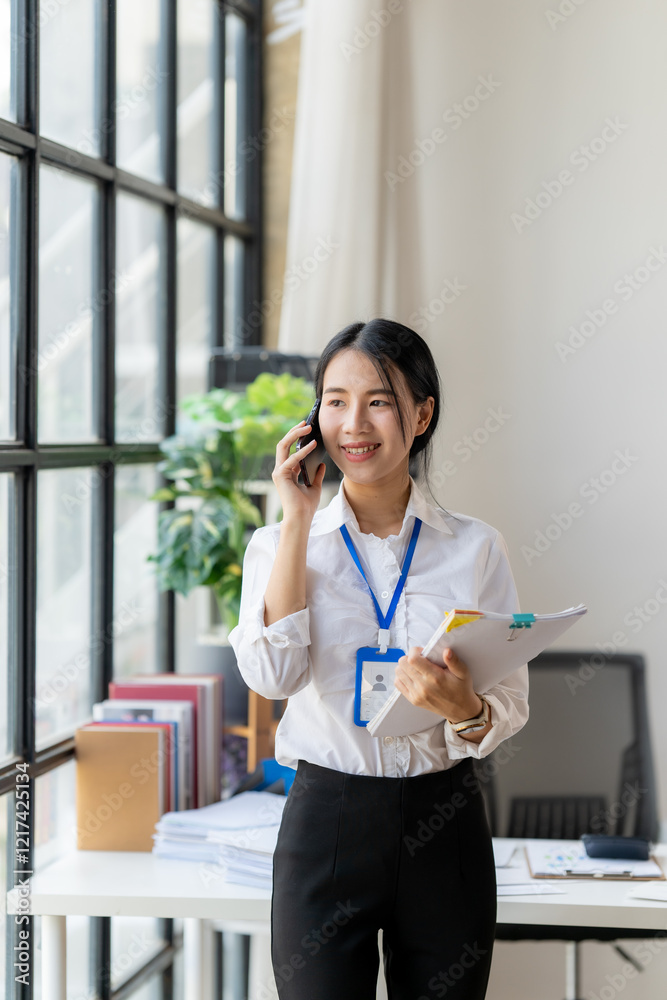 Professional on the Phone: A confident businesswoman with a warm smile, holding documents and talking on her phone in a modern office setting, radiates energy and efficiency, epitomizing success. Professional on the Phone: A confident businesswoman with a warm smile, holding documents and talking on her phone in a modern office setting, radiates energy and efficiency, epitomizing success.